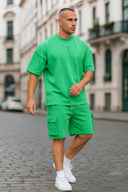 Man wearing a bright green outfit with shorts and a t-shirt on a city street.
