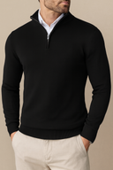 Man wearing a black quarter-zip sweater over a white shirt with beige pants on a beige background