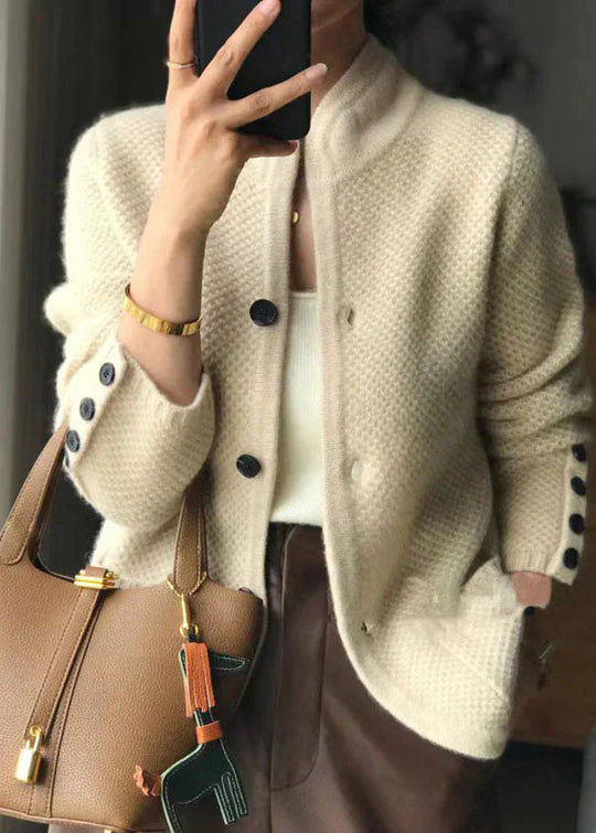 Person wearing a beige cardigan with black buttons, holding a brown handbag.