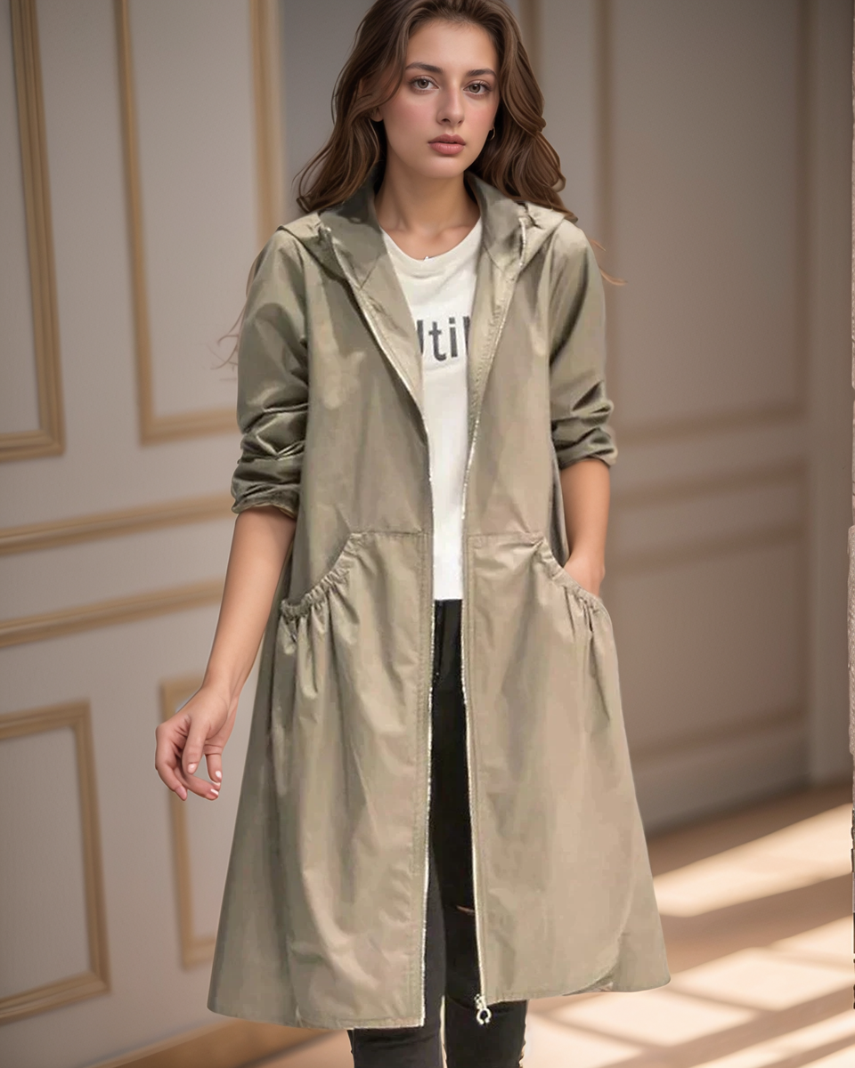 Woman wearing a long beige coat over a white shirt with text, standing indoors.