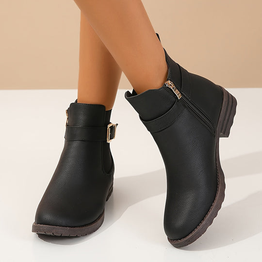 Black ankle boots with gold buckles on a beige background