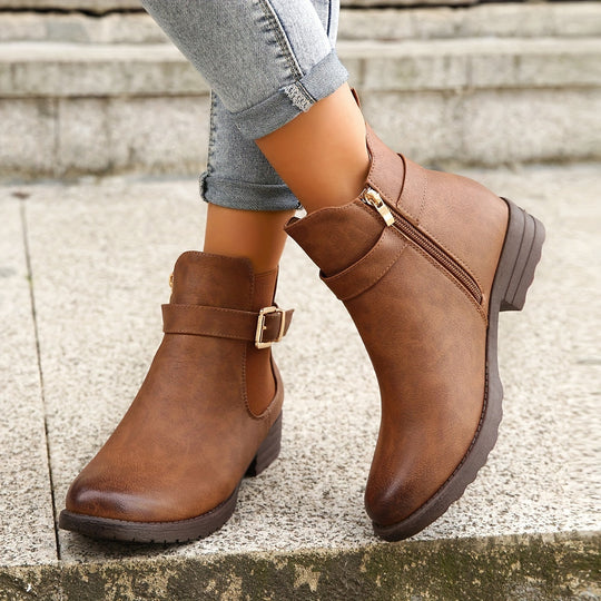 Brown ankle boots with buckles worn by a person on a concrete surface.