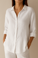 Person wearing a white button-up shirt with rolled-up sleeves against a beige background