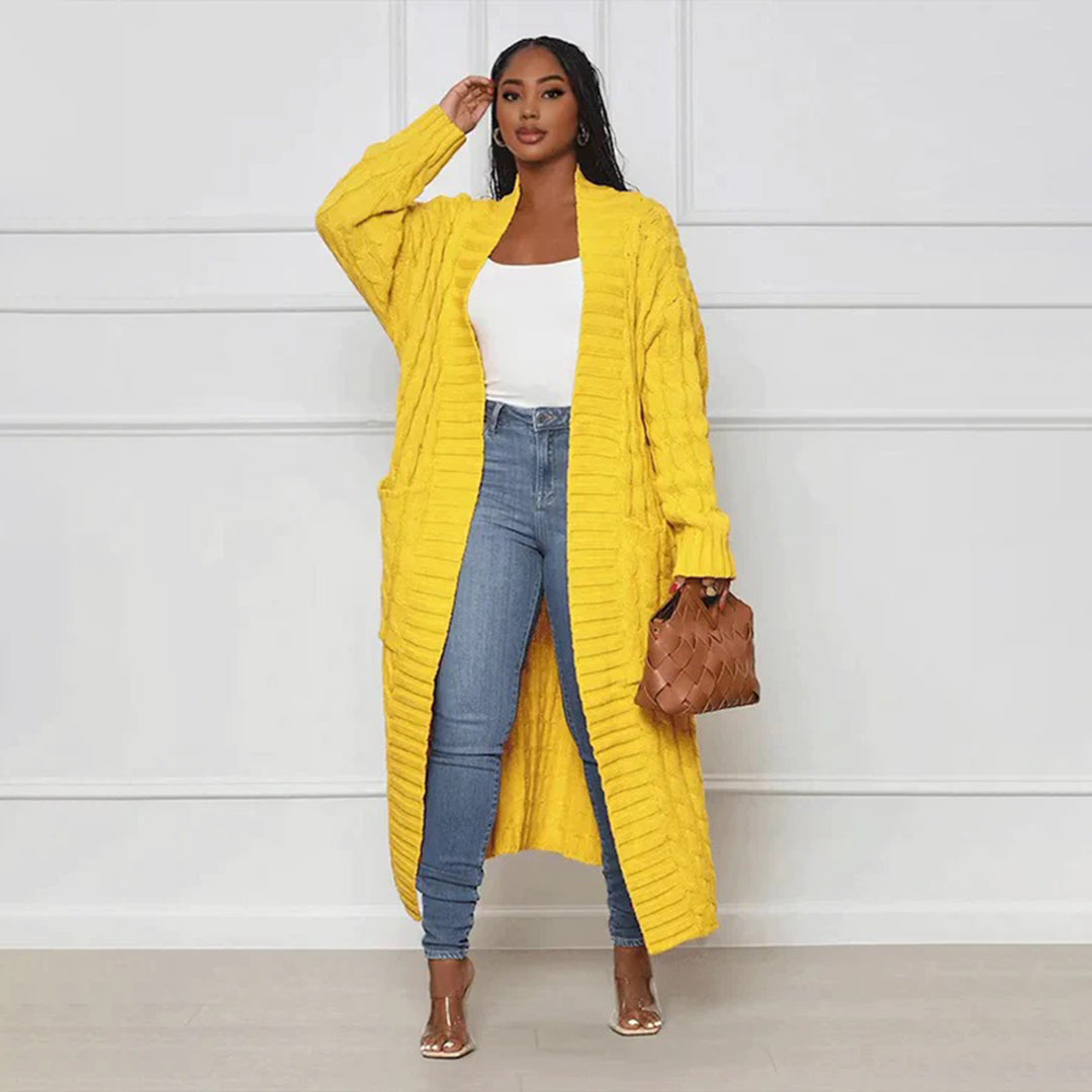 Woman wearing a bright yellow long coat over a white top and blue jeans, holding a brown bag against a white background.