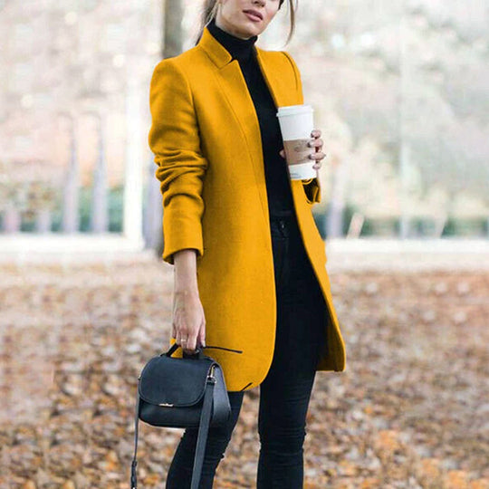 Woman wearing a mustard yellow coat holding a coffee cup outdoors.