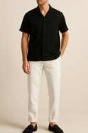 Person wearing a black short-sleeve shirt and white pants on a beige background