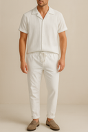 Man wearing a white striped shirt and white pants with beige shoes on a beige background