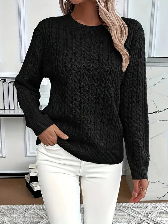 Person wearing a black cable knit sweater and white pants in an indoor setting.