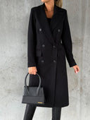 Person wearing a black coat holding a black handbag against a gray background