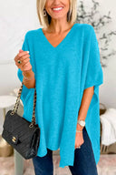 Woman wearing a blue poncho holding a black handbag indoors.