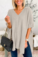 Woman wearing a gray poncho holding a black handbag indoors.