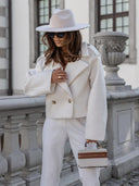 Woman in a white outfit with a hat and sunglasses, standing in front of classical architecture.