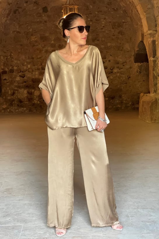 Woman in gold satin outfit standing in a rustic interior setting