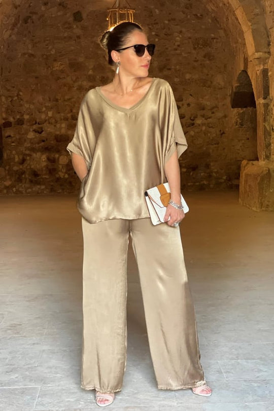 Woman in gold satin outfit standing in a rustic interior setting
