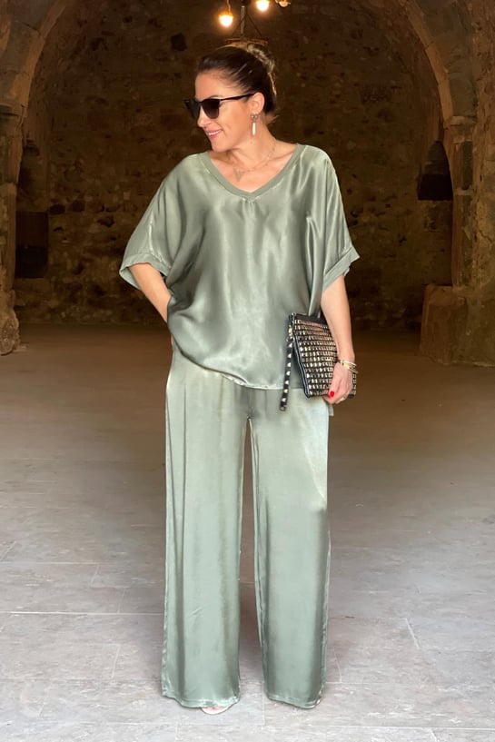 Woman in a green satin outfit standing in a stone-walled room.