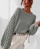 Woman wearing a gray knit sweater with textured sleeves against a white background