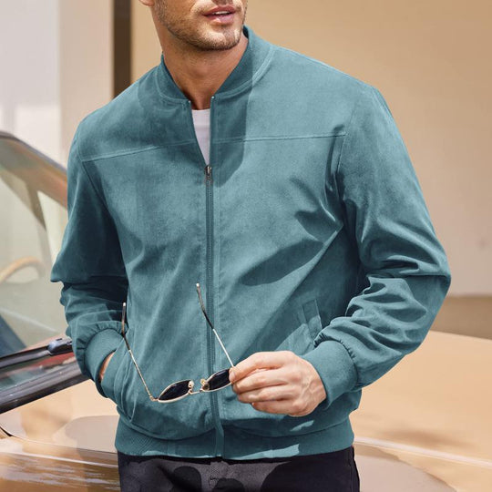 Man wearing a teal jacket holding sunglasses, standing next to a car.