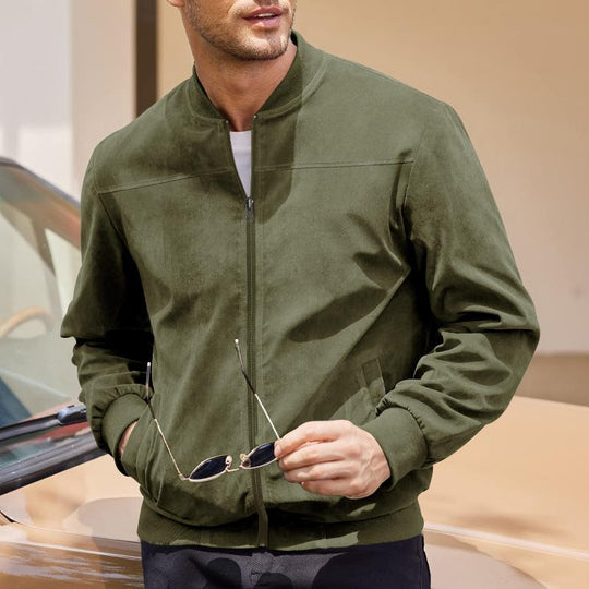 Man wearing a green bomber jacket holding sunglasses, standing next to a car.