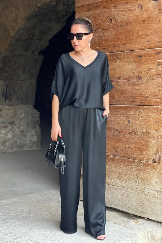 Woman in a black outfit standing against a wooden wall.